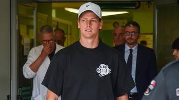 Jannik Sinner opuszcza budynek, ubrany w czarną koszulkę i białą czapkę z daszkiem.