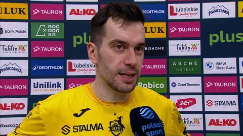 Marcin Komenda, zawodnik w żółtej koszulce sportowej, na tle sponsorów.