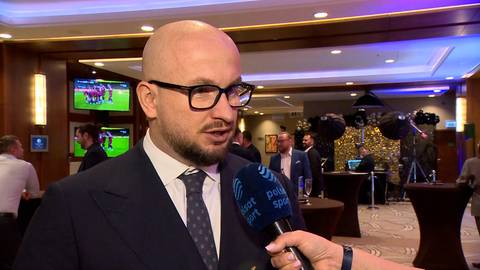 Tomasz Fornal, polski siatkarz, udziela wywiadu w eleganckim stroju. W tle widoczne są ekrany z transmisjami sportowymi i inni uczestnicy wydarzenia.