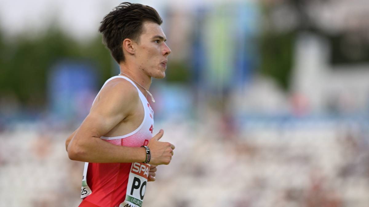 Polski lekkoatleta w białej koszulce z czerwonymi pasami biegnie.