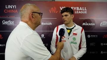 Mężczyzna w okularach i białej koszulce z mikrofonem rozmawia z młodym sportowcem w bluzie z polskim godłem i logo VNL.