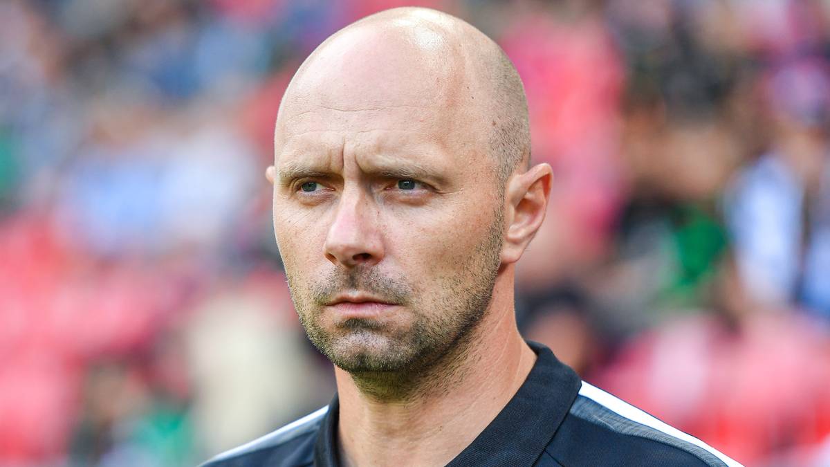 Portret mężczyzny, trenera piłkarskiego, w czarnej koszulce polo z herbem drużyny.