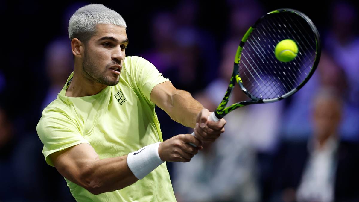 Carlos Alcaraz podczas meczu tenisowego, w żółtej koszulce, wykonujący zamach rakietą z piłką.