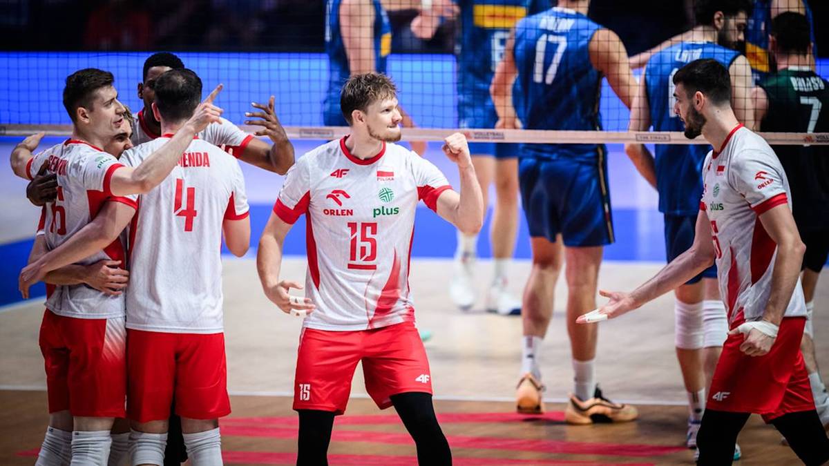 Siatkarze w biało-czerwonych strojach świętują, niektórzy się przytulają, inni unoszą ręce w górze. Widoczni są numery na koszulkach: 15, 4. Jeden z graczy trzyma w dłoni medalion. Tło to boisko do siatkówki.