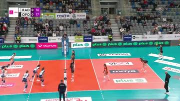 Rozgrywka siatk&oacute;wki kobiet na boisku. Zawodniczki w akcji, widoczna siatka, trybuny z kibicami oraz wynik meczu na telebimie.