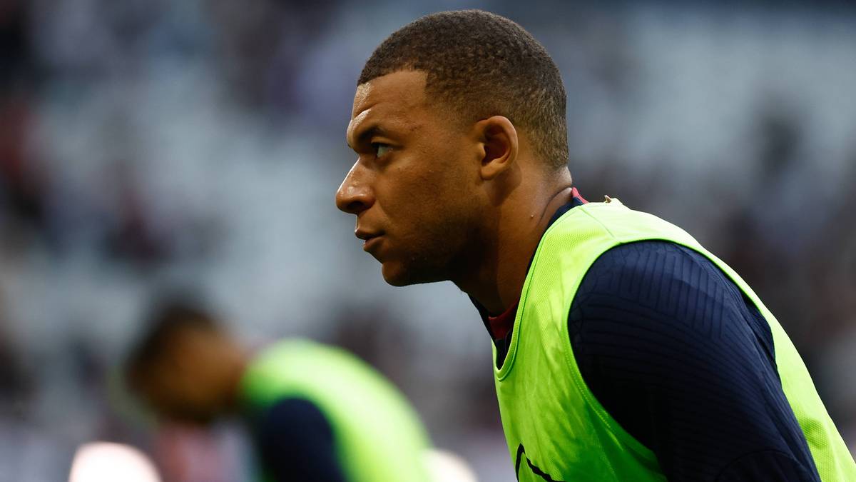 Kylian Mbappe, piłkarz PSG, w żółtej kamizelce treningowej, patrzy w bok z poważnym wyrazem twarzy.