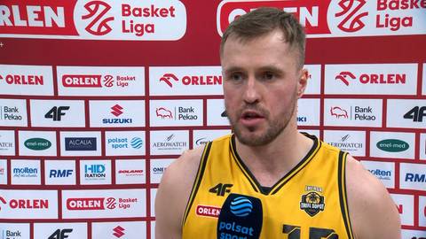 Mikołaj Witliński, koszykarz w ż&oacute;łtej koszulce z numerem 15, z kr&oacute;tką brodą, udziela wywiadu. W tle znajduje się ściana z logotypami ORLEN Basket Ligi i innych sponsor&oacute;w.