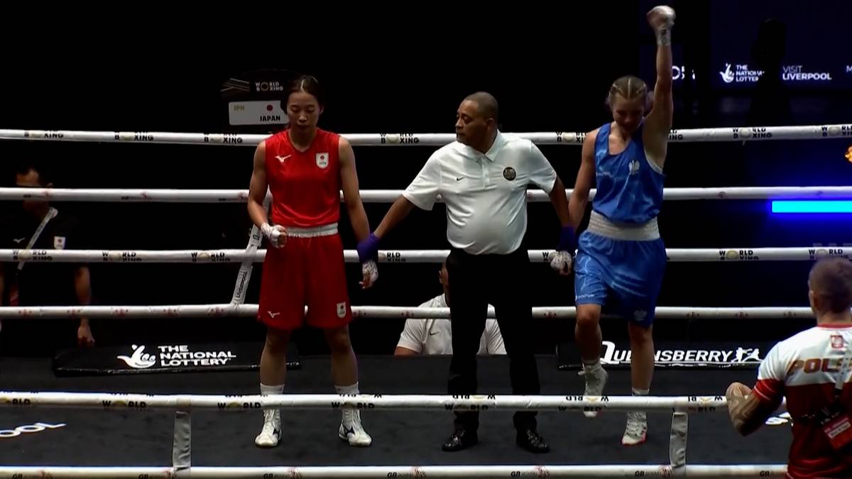 Bokserka w niebieskim stroju z uniesioną ręką stoi na ringu bokserskim obok bokserki w czerwonym stroju i sędziego. Bokserka w niebieskim stroju świętuje zwycięstwo.