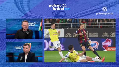 Dw&oacute;ch piłkarzy w akcji na boisku, jeden pr&oacute;buje odebrać piłkę drugiemu. W tle trybuny stadionu.