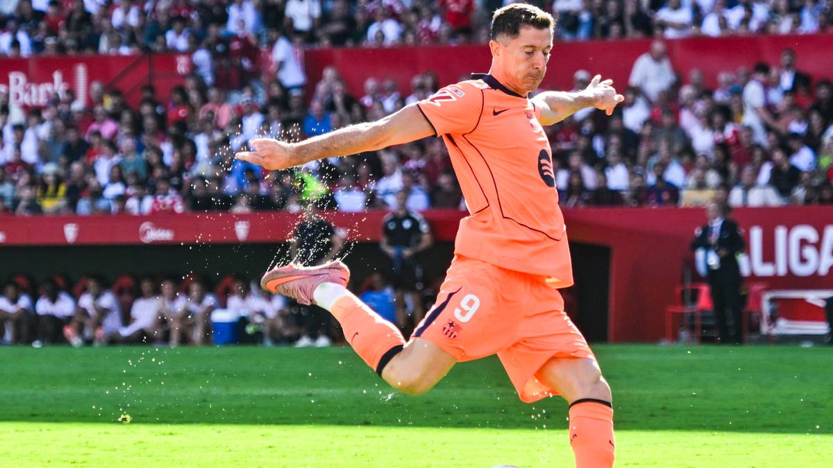 Piłkarz Robert Lewandowski w pomarańczowym stroju wykonuje kopnięcie piłki na zielonym boisku.