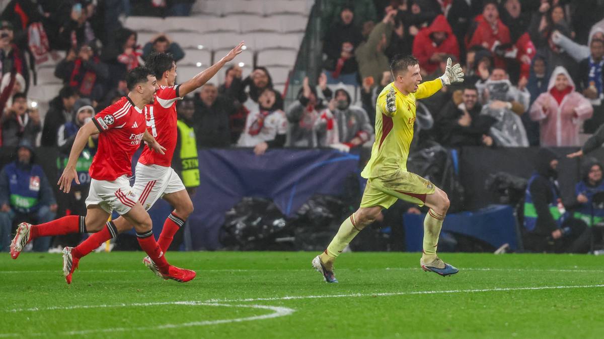 Piłkarze w czerwonych strojach biegną po boisku, jeden z nich próbuje odebrać piłkę bramkarzowi.