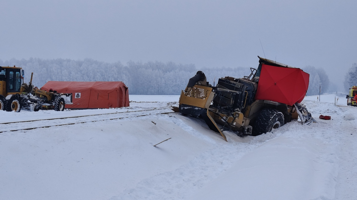 Zniszczona koparka leżąca na boku obok tor&oacute;w kolejowych w zimowej scenerii, obok stoi namiot medyczny.
