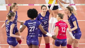 Grupa siatkarek w niebieskich strojach świętuje zdobycie punktu na boisku siatkarskim.