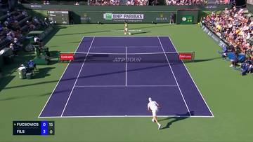 Widok z g&oacute;ry na kort tenisowy podczas meczu, z dwoma zawodnikami w akcji i widoczną tablicą wynik&oacute;w.