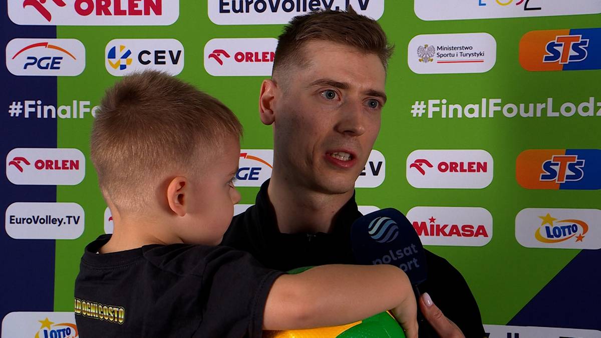 Siatkarz Mikołaj Semeniuk trzyma na rękach małe dziecko i udziela wywiadu przed kamerą.