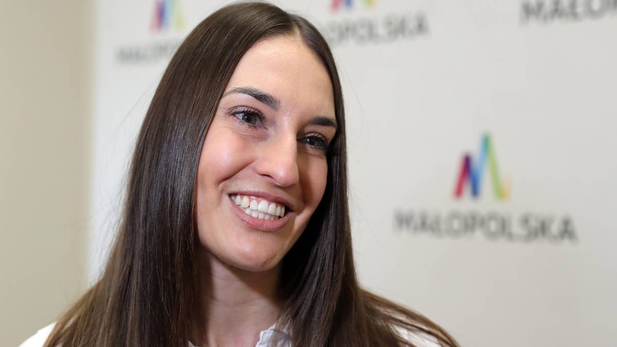 Uśmiechnięta młoda kobieta o ciemnych włosach, ubrana w białą koszulę.