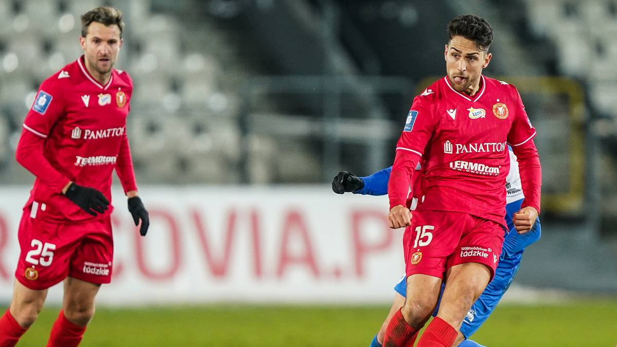 Dw&oacute;ch piłkarzy w czerwonych strojach Widzewa Ł&oacute;dź na boisku, jeden z numerem 25, drugi z numerem 15 na spodenkach.