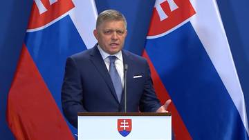 Premier Słowacji Robert Fico przemawia za m&oacute;wnicą z herbem Słowacji, w tle flagi Słowacji.