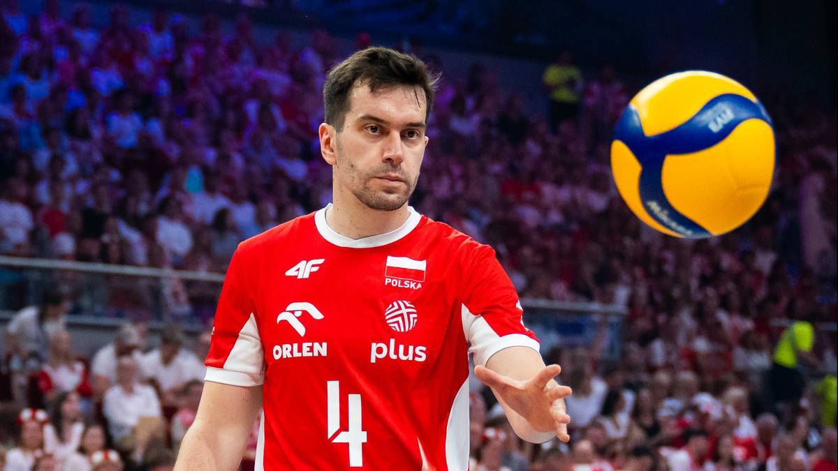 Marcin Komenda, polski siatkarz, w czerwonej koszulce z białym orłem i biało-czerwoną flagą, z piłką do siatk&oacute;wki w tle