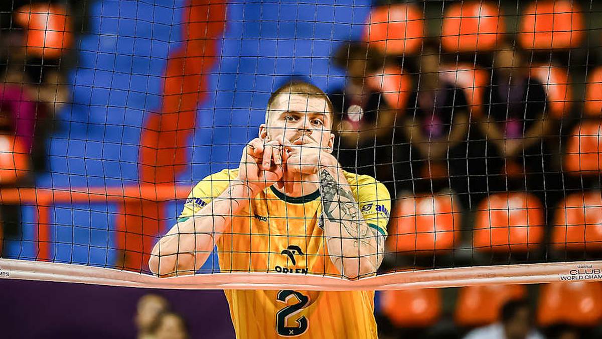 Siatkarz w ż&oacute;łtej koszulce z numerem 2 na plecach, z rękami przy twarzy, stoi przy siatce.