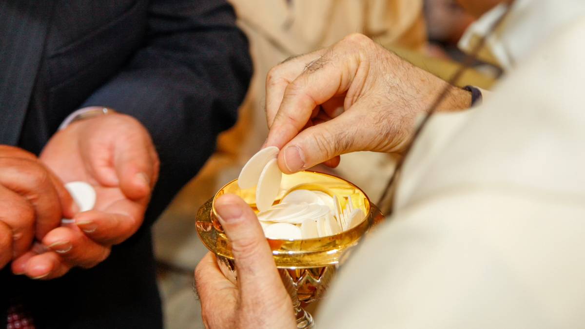 Ręka kapłana podaje hostię wiernemu z kielicha podczas Komunii Świętej.