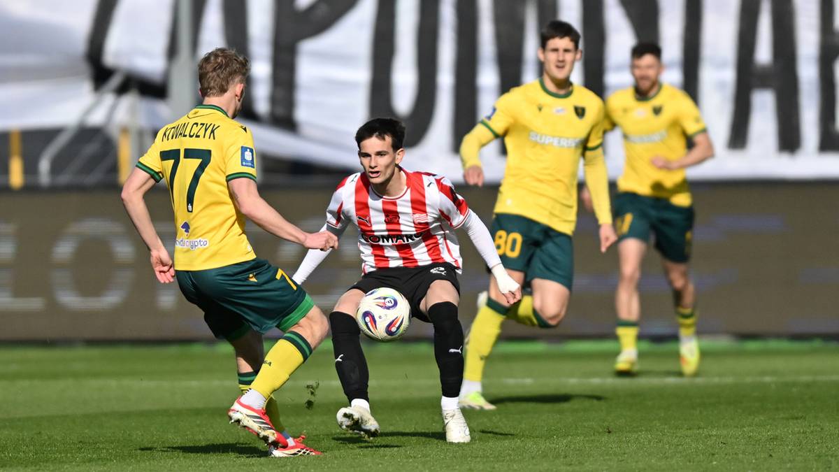 Czterech piłkarzy na boisku podczas meczu, trzech w żółtych strojach, jeden w biało-czerwonej koszulce, walczą o piłkę.