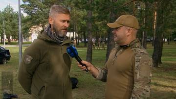 Siergiej Senyk w zielonym mundurze udziela wywiadu na tle lasu.
