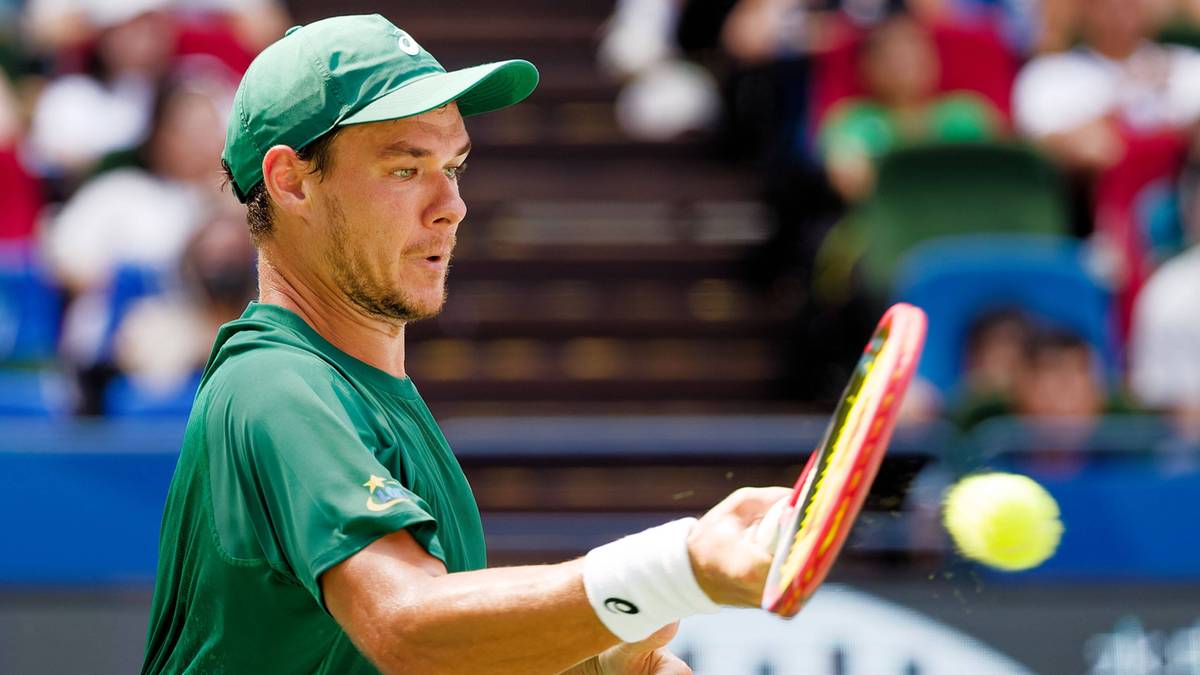 Tenisista w zielonej czapce i koszulce z rakietą w ręku, przygotowuje się do odbicia piłki.