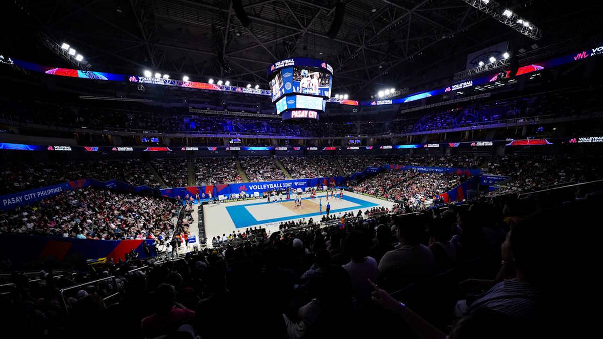 Siatkarska hala podczas meczu, z widownią wypełniającą trybuny, oświetlona jarzeni&oacute;wkami i z kolorowymi światłami na suficie.