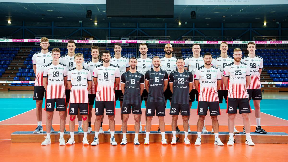 Drużyna siatkarska Asseco Resovii w komplecie, stojąca w dwóch rzędach na parkiecie hali sportowej, ubrana w biało-czarne stroje meczowe.