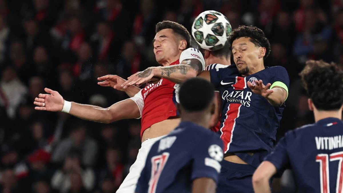 Dwóch piłkarzy walczy o górną piłkę podczas meczu piłki nożnej. Jeden z nich jest ubrany w czerwoną koszulkę, drugi w granatową.