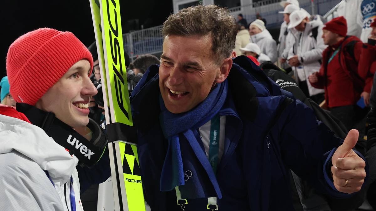 Dw&oacute;ch mężczyzn, jeden w czerwonej czapce i białej kurtce, drugi w ciemnej kurtce i szaliku, rozmawia podczas wydarzenia sportowego.