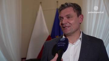 Adam Korol, były minister sportu, udziela wywiadu przed polskimi i unijnymi flagami.