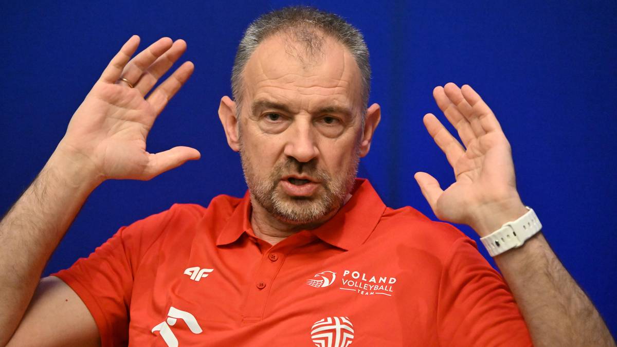 Mężczyzna w czerwonej koszulce z białym nadrukiem, podnoszący ręce w geście m&oacute;wienia lub podkreślania swoich sł&oacute;w.
