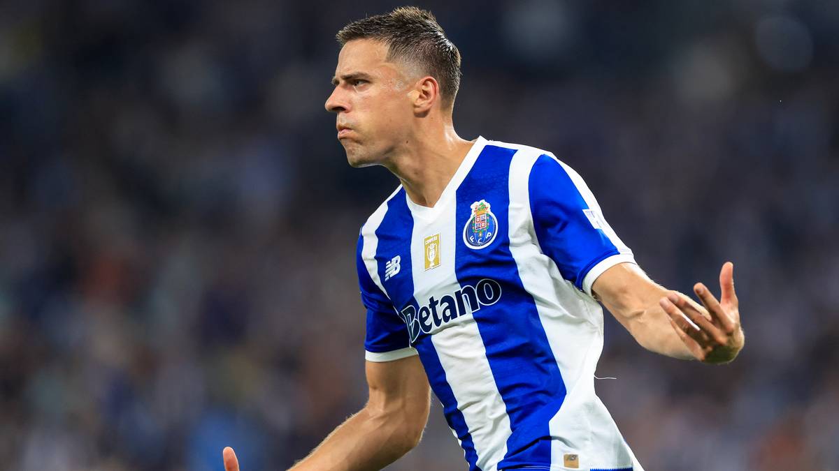 Piłkarz FC Porto w białej i niebieskiej koszulce, patrzący w bok z uniesionymi rękami.