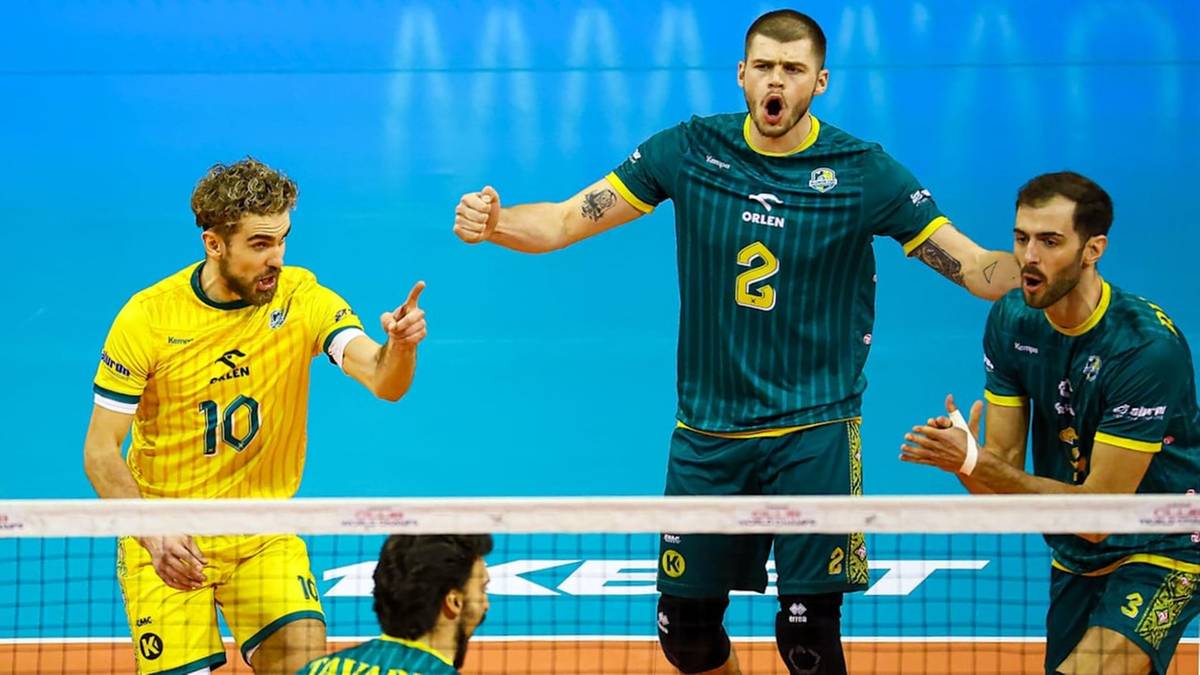 Trzech siatkarzy w akcji podczas meczu siatk&oacute;wki, z zawodnikiem w zielonej koszulce numer 2 w centrum.