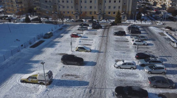 Zimowy widok na osiedle mieszkaniowe z zaparkowanymi na śniegu samochodami na otwartym parkingu.