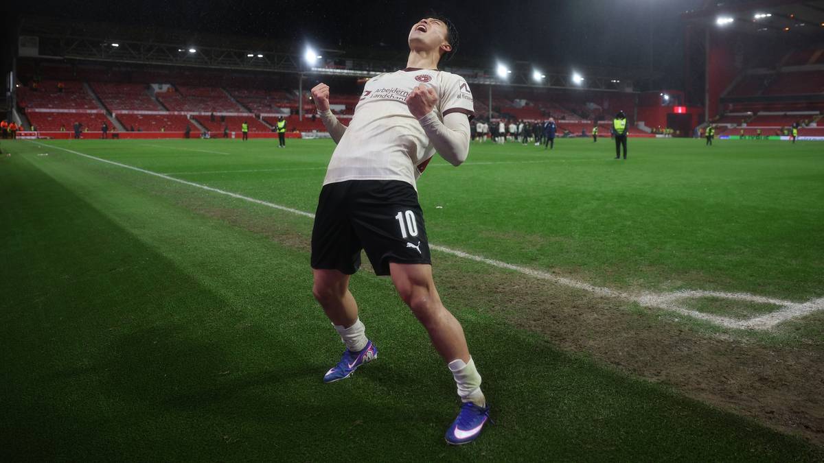 Piłkarz w białej koszulce i czarnych spodenkach cieszy się po strzelonej bramce na boisku piłkarskim.