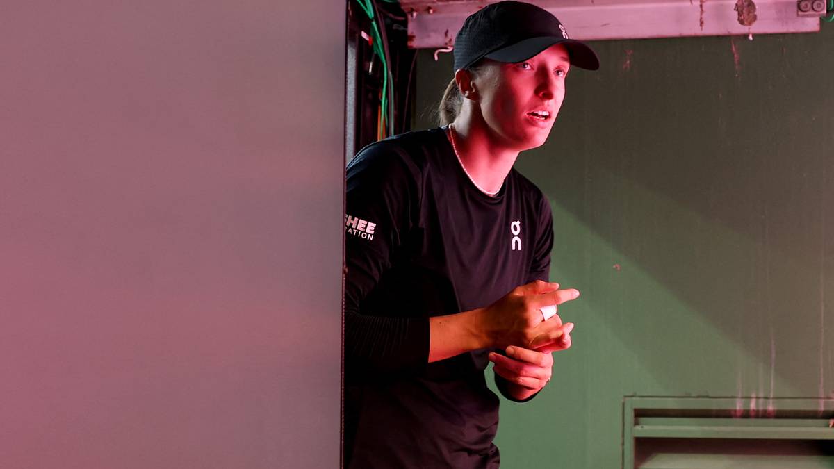 Kobieta w czapce i stroju tenisowym trzyma piłkę, patrząc w bok.