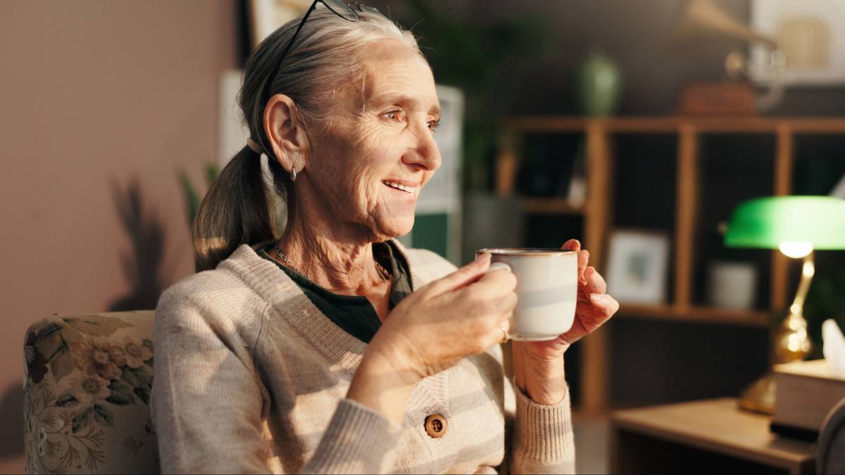 Uśmiechnięta starsza kobieta trzymająca kubek z napojem.