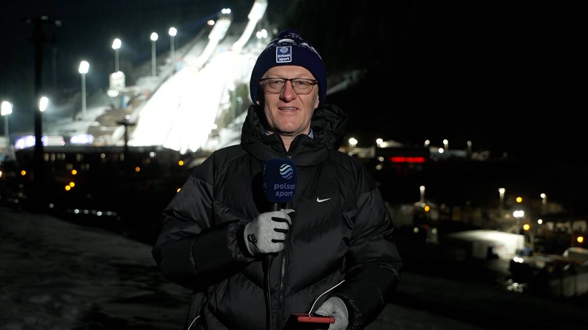 Mężczyzna w czapce i okularach, ubrany w zimową kurtkę, trzyma mikrofon z logo "Eurosport" i uśmiecha się do kamery. W tle widać oświetloną skocznię narciarską nocą.