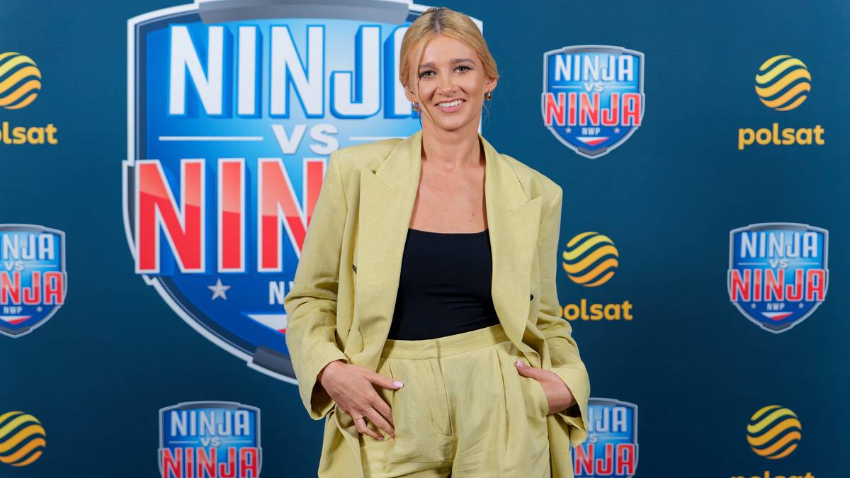 Kobieta w żółtym garniturze, Marta Ćwiertniewicz, stoi na tle niebieskiej tablicy z napisem "Ninja vs Ninja".