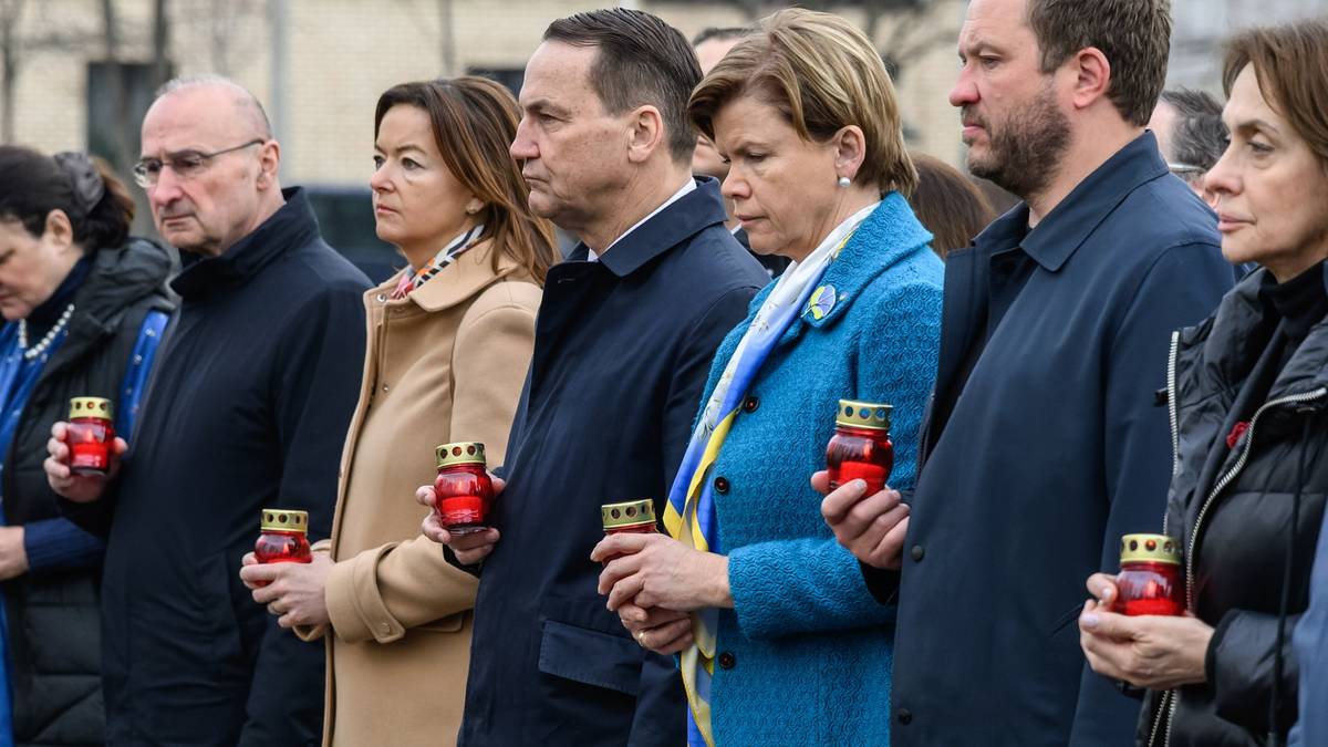 Grupa polityków trzymających w dłoniach zapalone znicze podczas uroczystości.