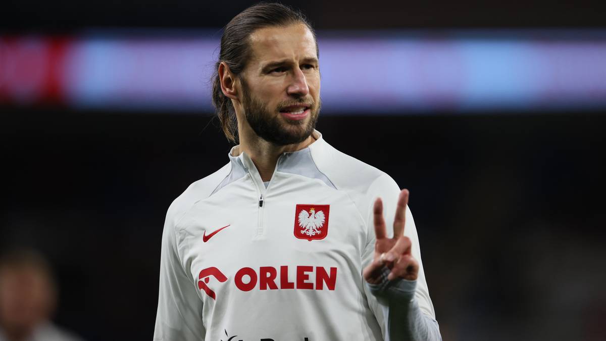 Piłkarz Grzegorz Krychowiak w białej koszulce reprezentacji Polski z orłem i logo "ORLEN" pokazuje dwa palce.