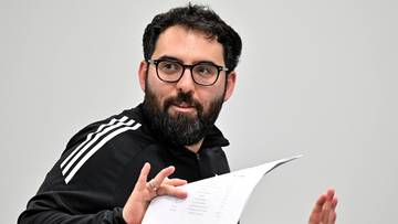 Portret Goncalo Feio, mężczyzny z brodą i okularami, kt&oacute;ry trzyma w rękach kartkę papieru i gestykuluje.