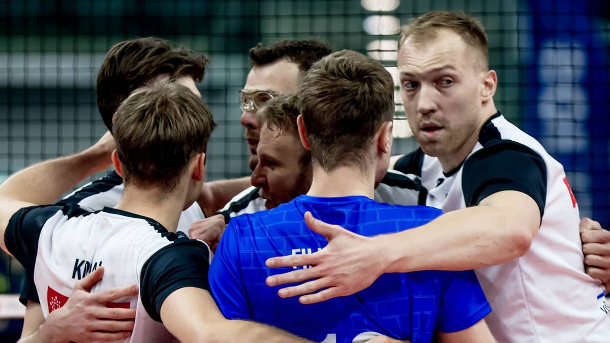 Drużyna siatkarzy w białych i niebieskich strojach sportowych przytulająca się nawzajem, symbolizująca jedność zespołową.