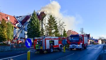 Samochody strażackie przy płonącym budynku, z kt&oacute;rego wydobywa się dym.