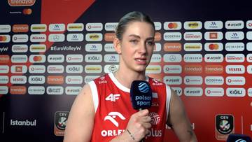 Magdalena Stysiak w czerwonym stroju reprezentacji Polski udziela wywiadu trzymając mikrofon Polsat Sport na tle ścianki sponsorskiej.
