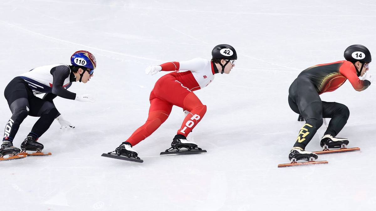 Trzech łyżwiarzy szybkich w kaskach i strojach sportowych na lodowym torze podczas zawod&oacute;w.