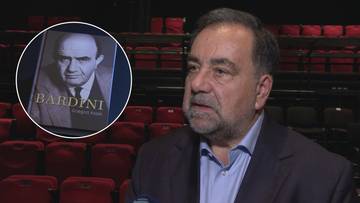 Dziennikarz Grzegorz Kozak na tle foteli teatralnych z widoczną okładką książki Bardini.